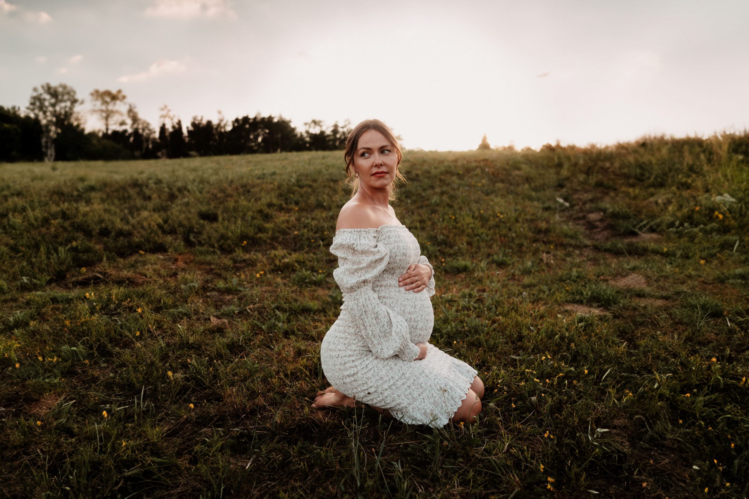 Frau sitzt auf Wiese bei einem Outdoor-Shooting und trägt ein Blumenkleid für Schwangere